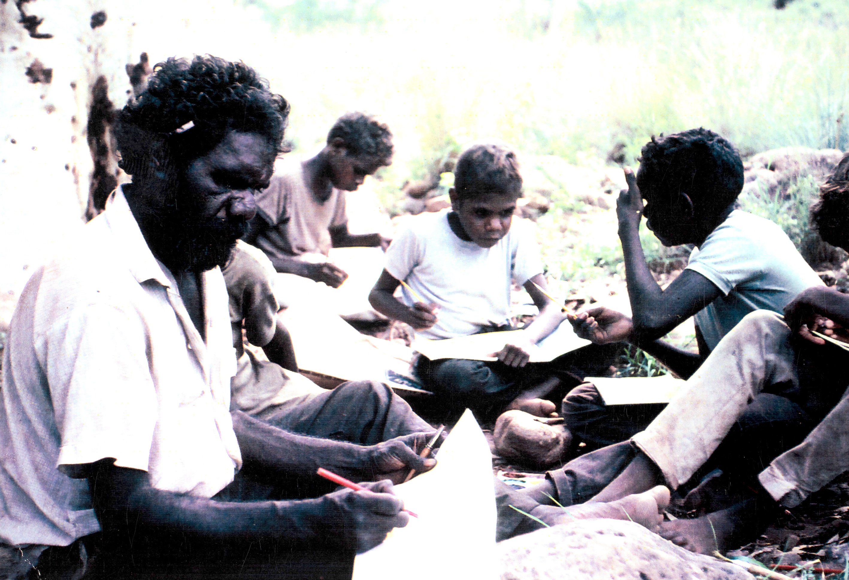Assistant Teacher with students sitting on ground working.